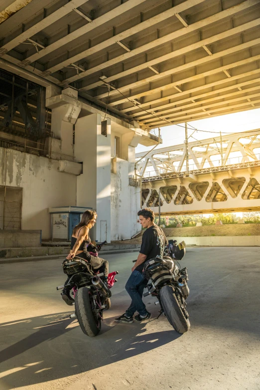 a man and a woman sitting on motorcycles under an overpass