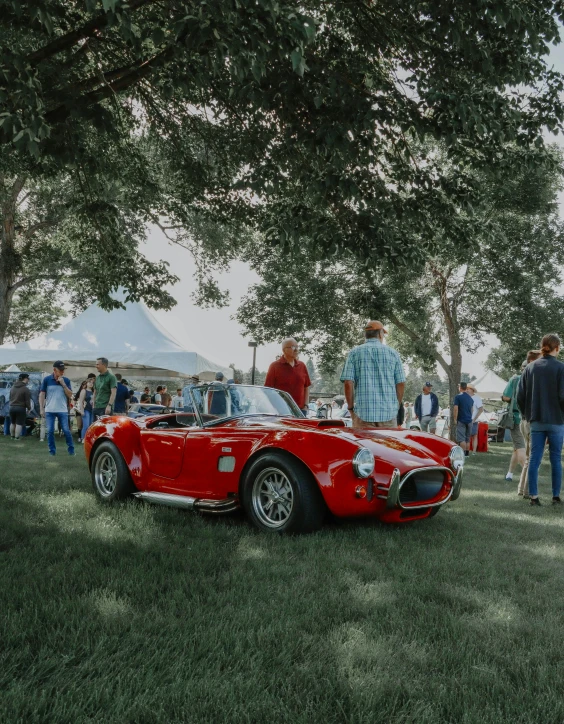 people gathered at an old classic show near an antique sports car