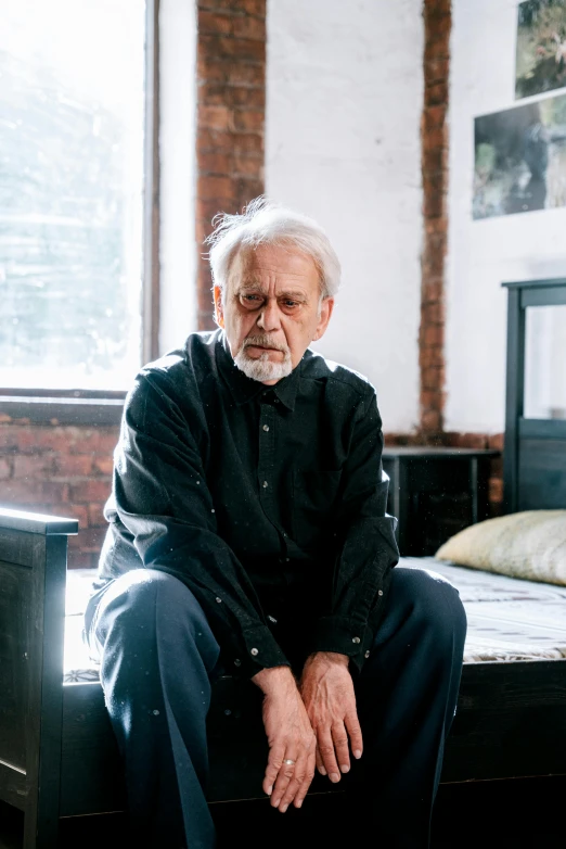 a man with grey hair sitting on a bench next to a bed