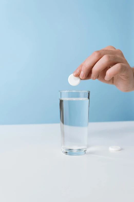hand holding pills above glass of water