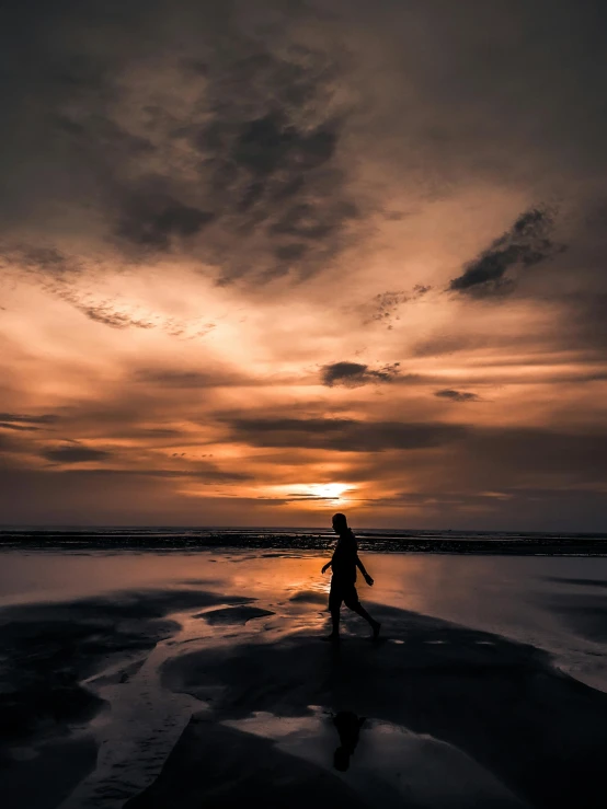 man with surfboard walking on sandy beach at sunset