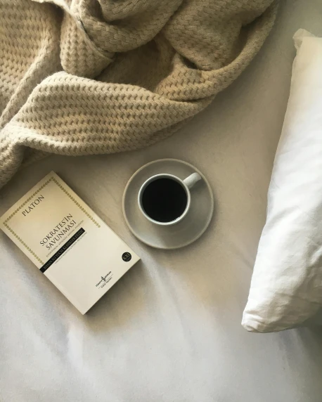 a book, cup of coffee and scarf on a bed