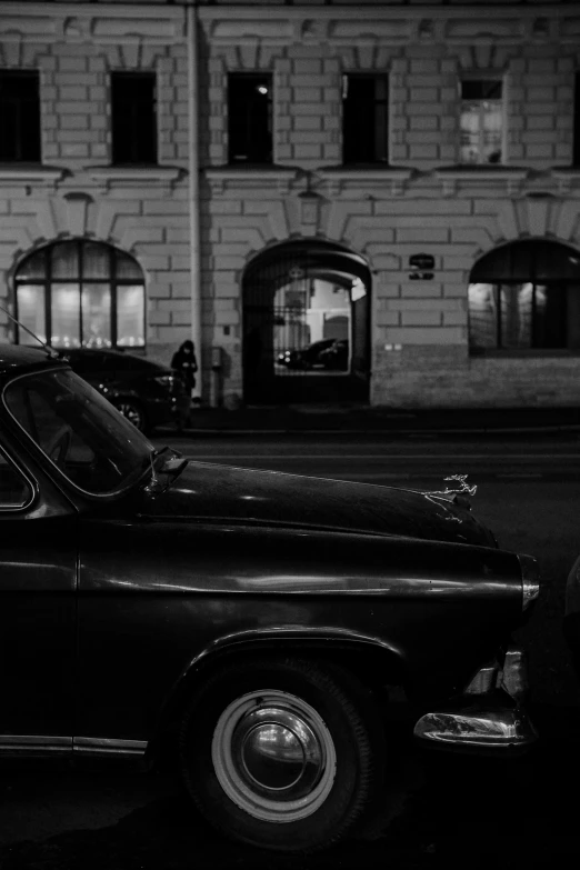 a old black car parked on the side of the road in front of a building