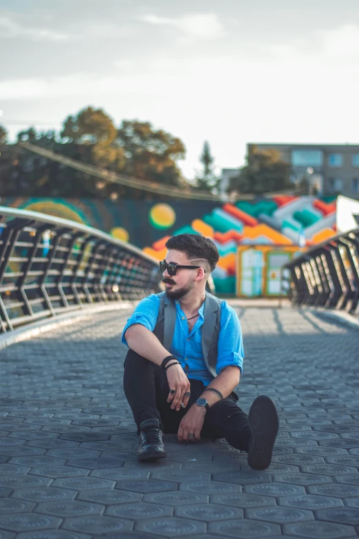 a man with dark brown hair, glasses and backpack sitting on a brick walkway