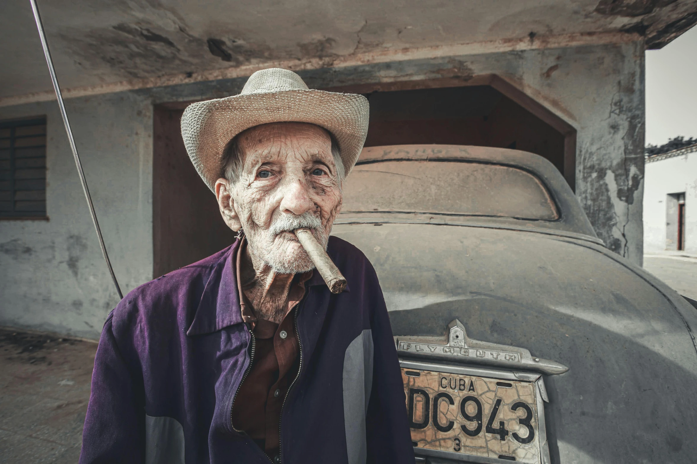 a man wearing a hat sitting next to an old car