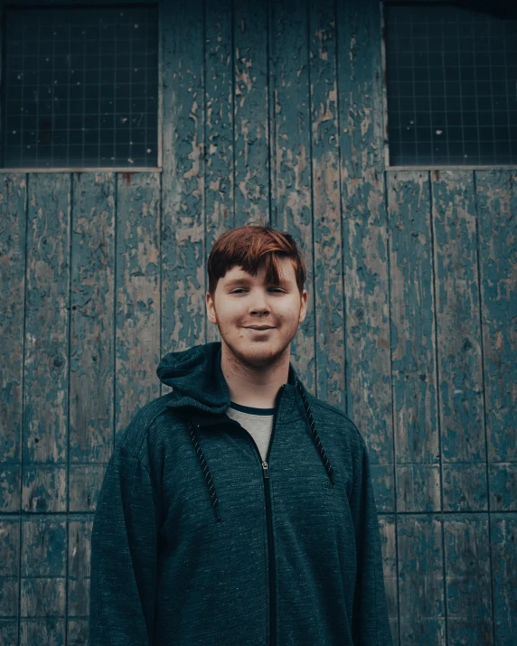 a man in blue jacket standing by wooden wall