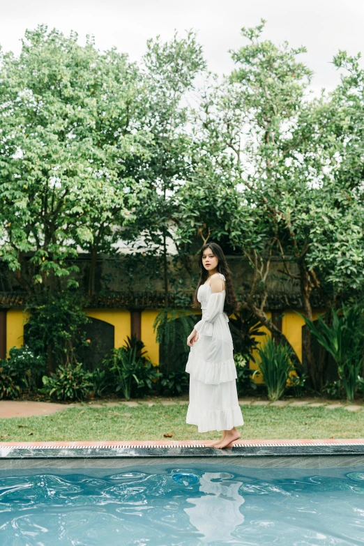 a woman in a white dress standing next to a pool