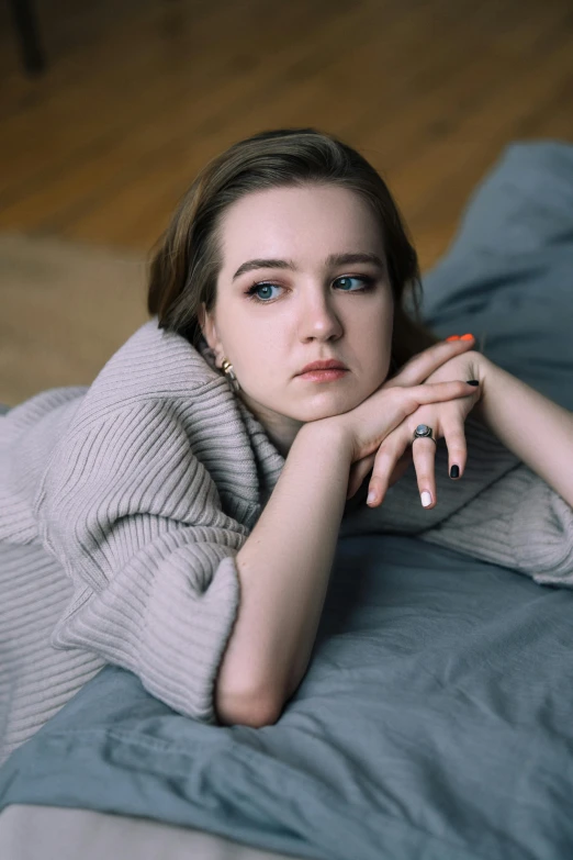 a woman wearing grey is laying on a bed