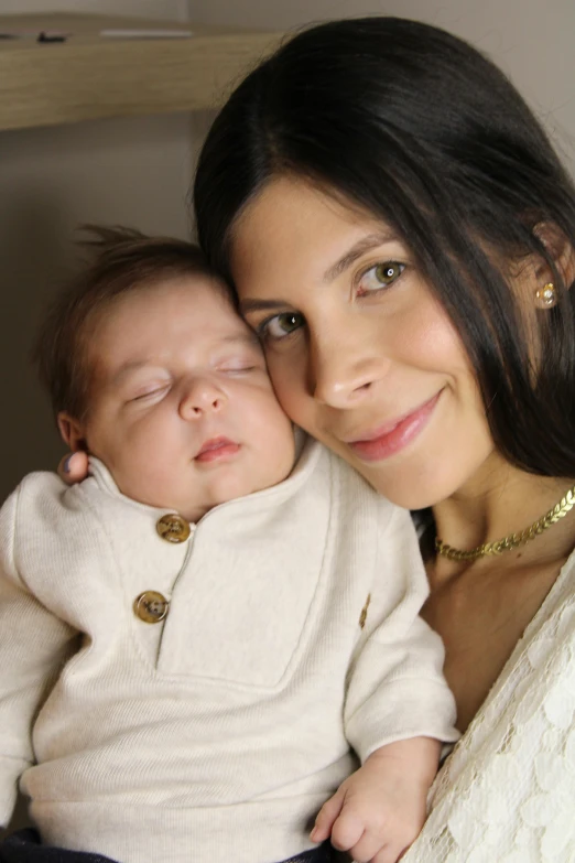 a woman in white sweater holding baby and smiling