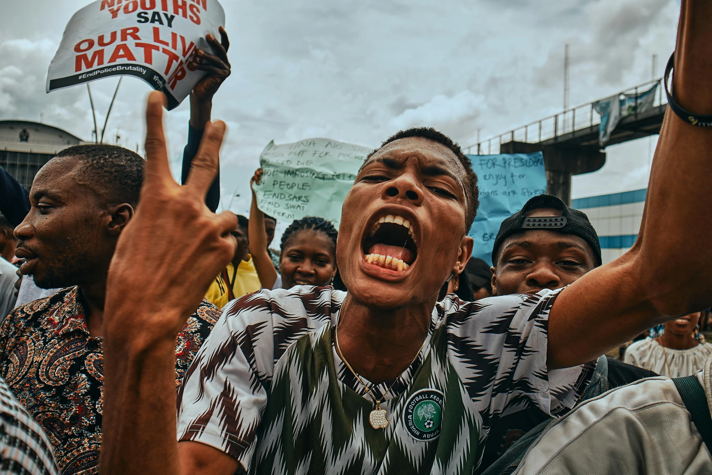 a man in a crowd celeting with a sign that says protest is our own mate