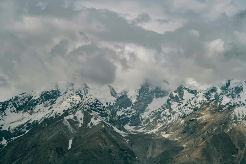 snow capped mountains with clouds above them on cloudy day