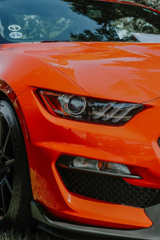 an orange mustang parked next to a forest