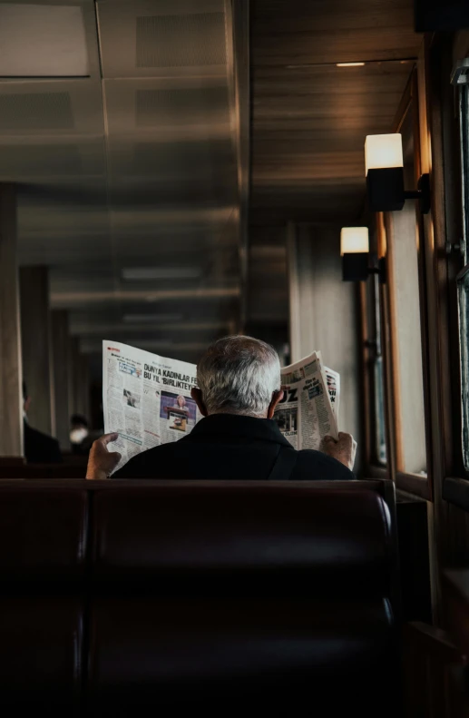 an old man sits on the train reading a newspaper