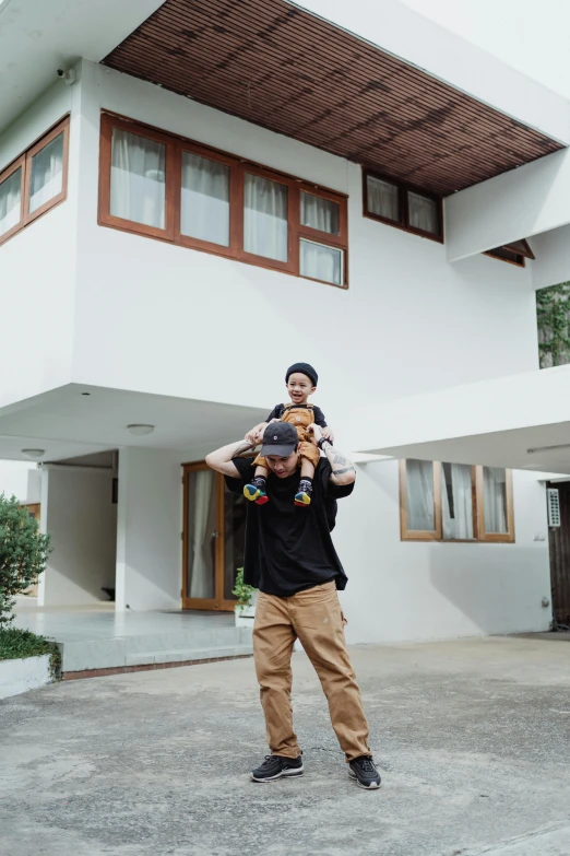 a man holds a baby up in front of a house