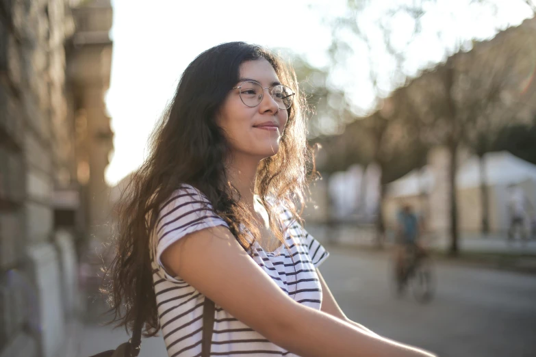 woman wearing glasses, leaning on wall near tree, during sun set