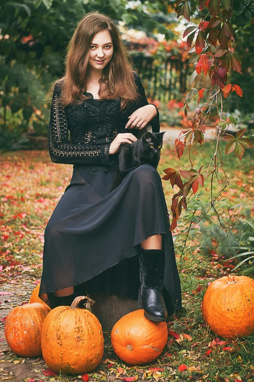 a woman holding a cat sits among three pumpkins