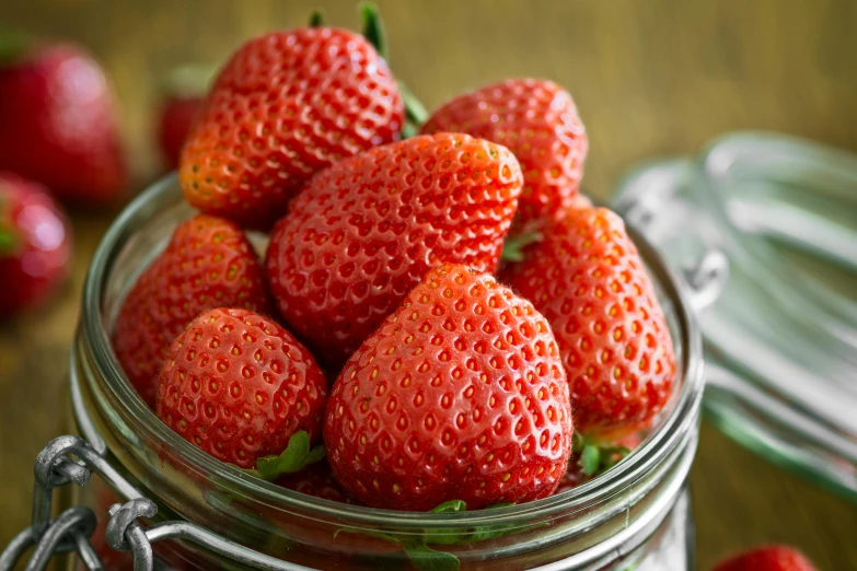 a bowl full of strawberries next to a jar with other ripe berries