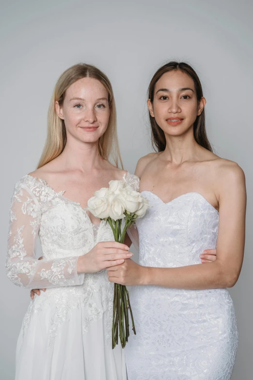 two brides pose for a pograph while one holds flowers