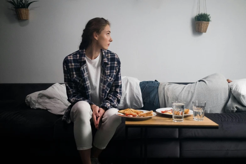 a woman sitting on a sofa with two glasses and plate of food