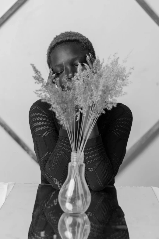 a woman covering her face next to a vase with dried plants