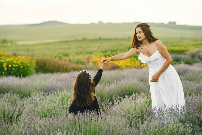 a beautiful woman in white is holding the hand of a little girl in a field of lavender flowers