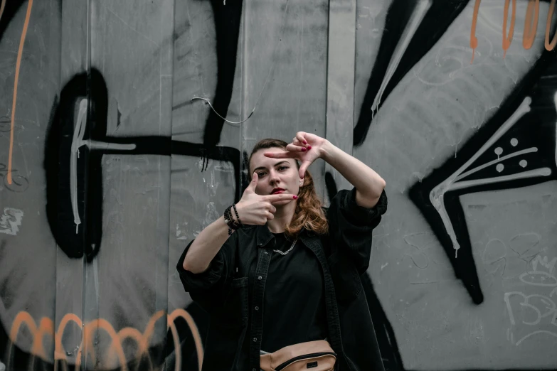 a woman stands in front of a wall that has some graffiti on it