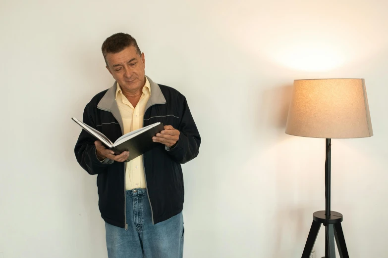 a man is reading a book while standing in front of a lamp