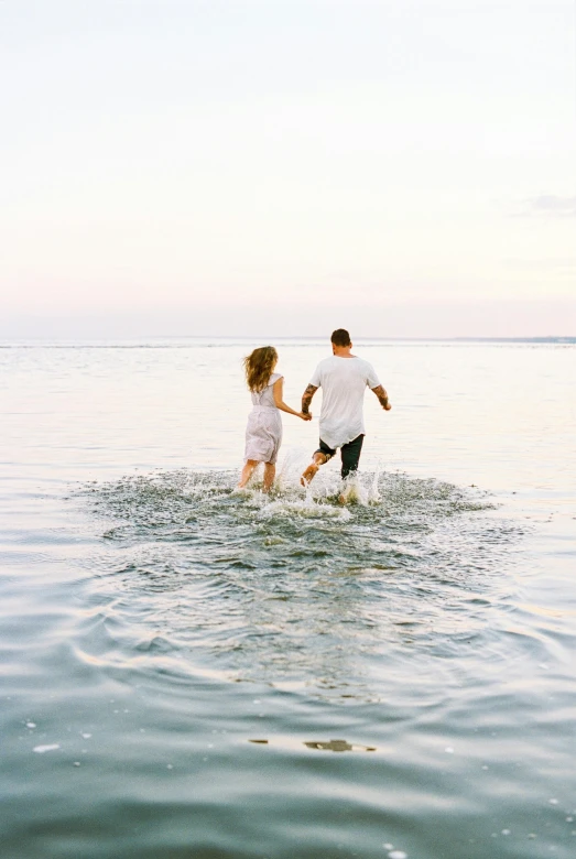 a man and woman walking into the water with one woman holding her leg