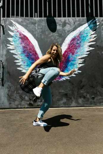 woman in blue leggings dancing with a painted wings on the wall