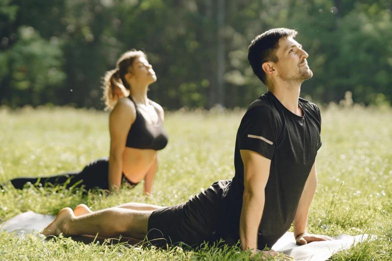 a man and woman are laying on yoga mats in a meadow