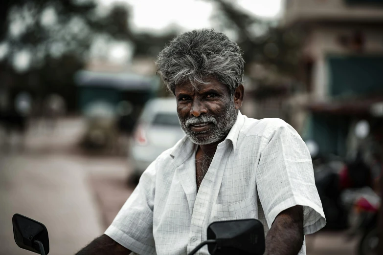 an old man with a beard sits on a motor scooter