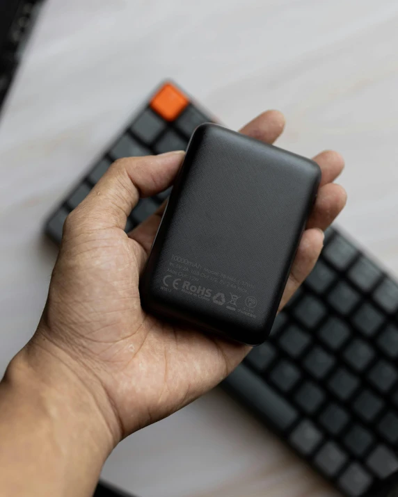 a person is holding an external hard drive next to a keyboard