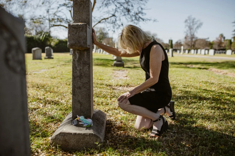 a young woman sitting by a cross in a cemetery