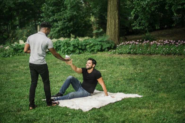 a man is sitting on a towel holding a bowl while the other one stands in the background