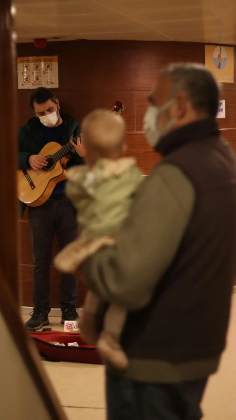 two men with masks and an infant playing guitar