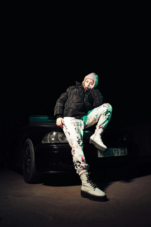 a man with black jacket and green pants sitting on a black car