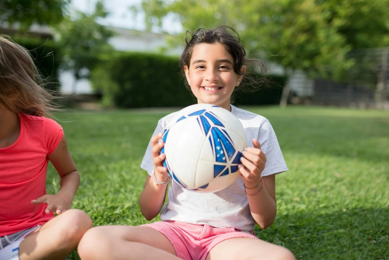 two girls sitting in the grass holding a soccer ball