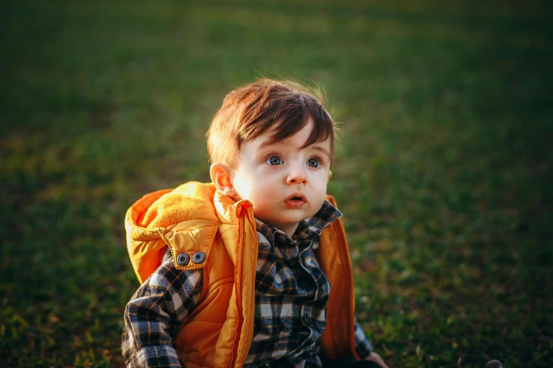 a toddler sits on the grass wearing a backpack