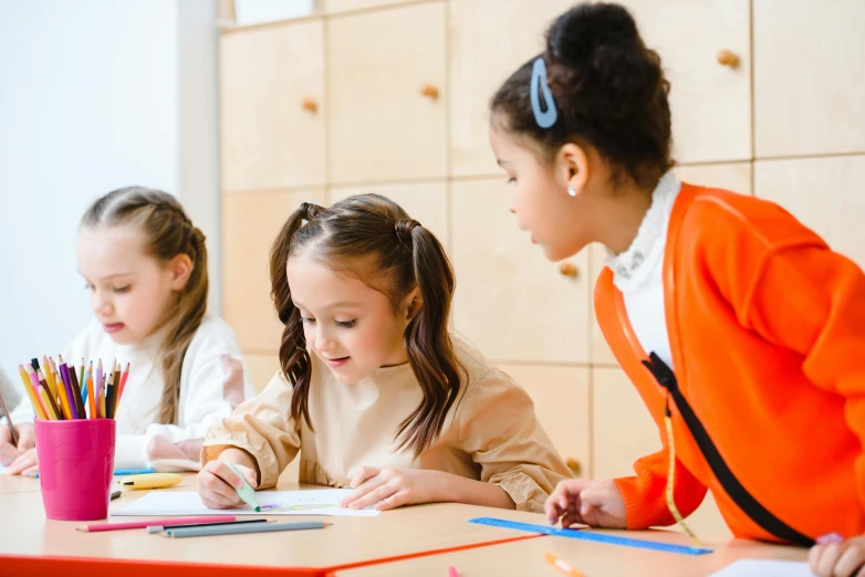 three children sitting at a table in front of colored pencils