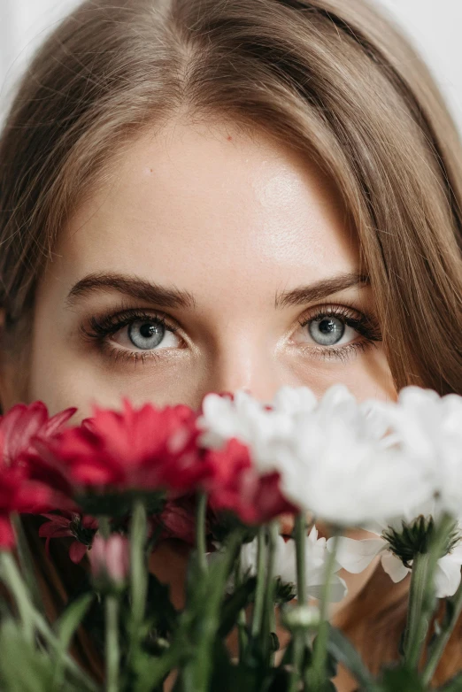 a woman with blue eyes stares over some red and white flowers