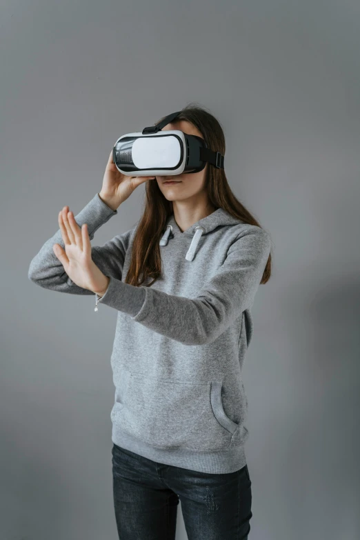 a  wearing a glasses and a sweater is holding her hand up while wearing a vr goggles