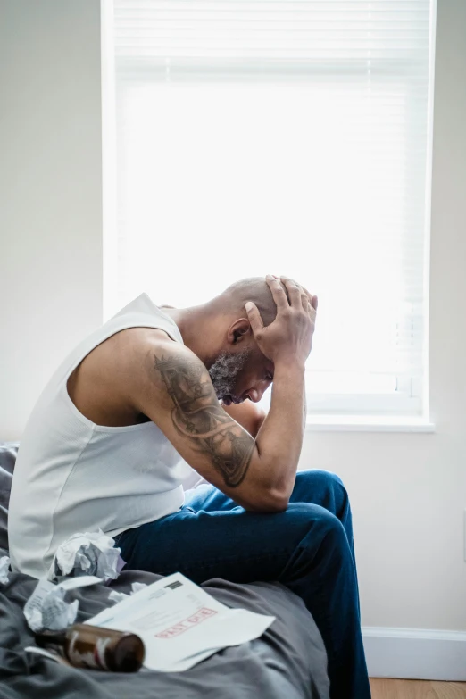 the man is sitting in front of a window holding his hands to his face