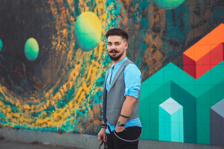 a man is posing in front of a wall that has a colorful painting