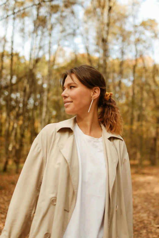 woman walking through woods in raincoat and earrings