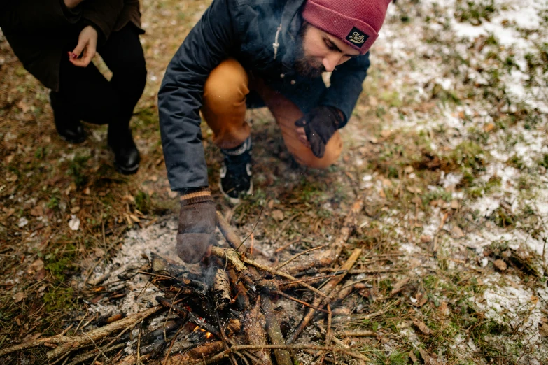 a person kneeling down in the snow next to a fire