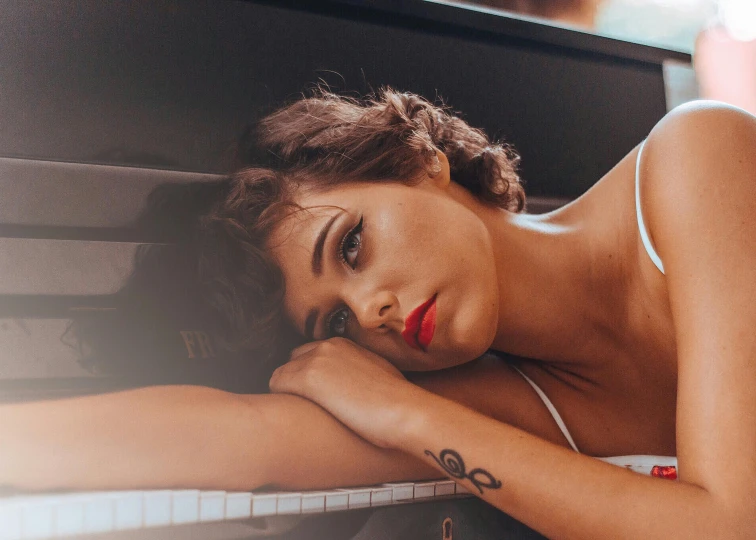 an image of a girl in lingerie lying her head on a piano