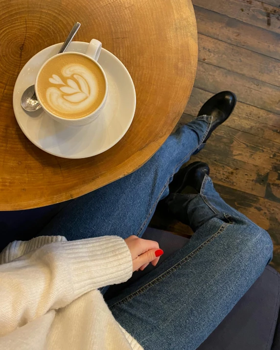 the legs and ankles of a person in a sweater, dark booties and a cappuccino