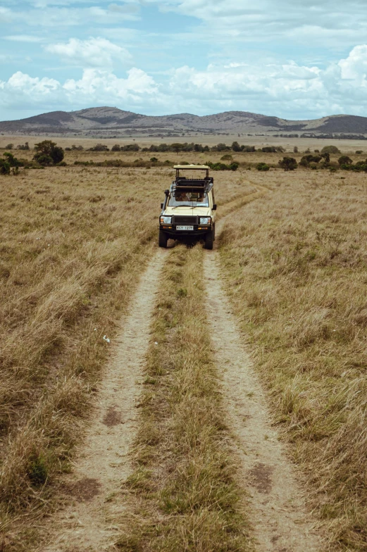 a vehicle on the side of a dirt road in a dry grass field