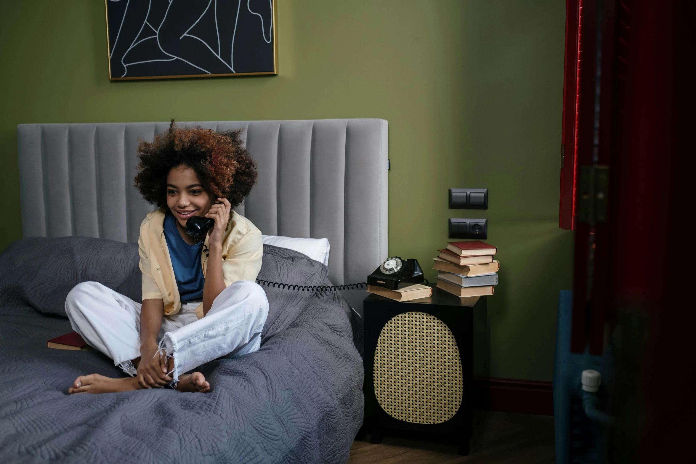 a smiling woman sitting on her bed while talking on the phone