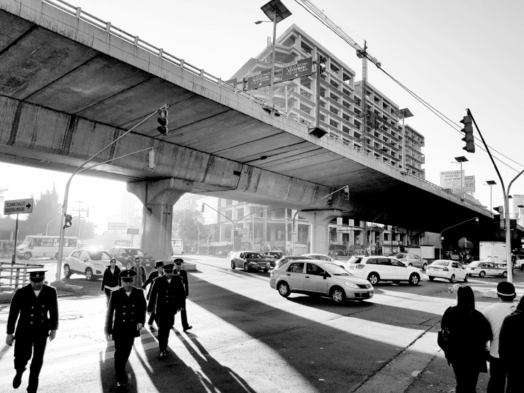 people walk past traffic under an overpass on a sunny day